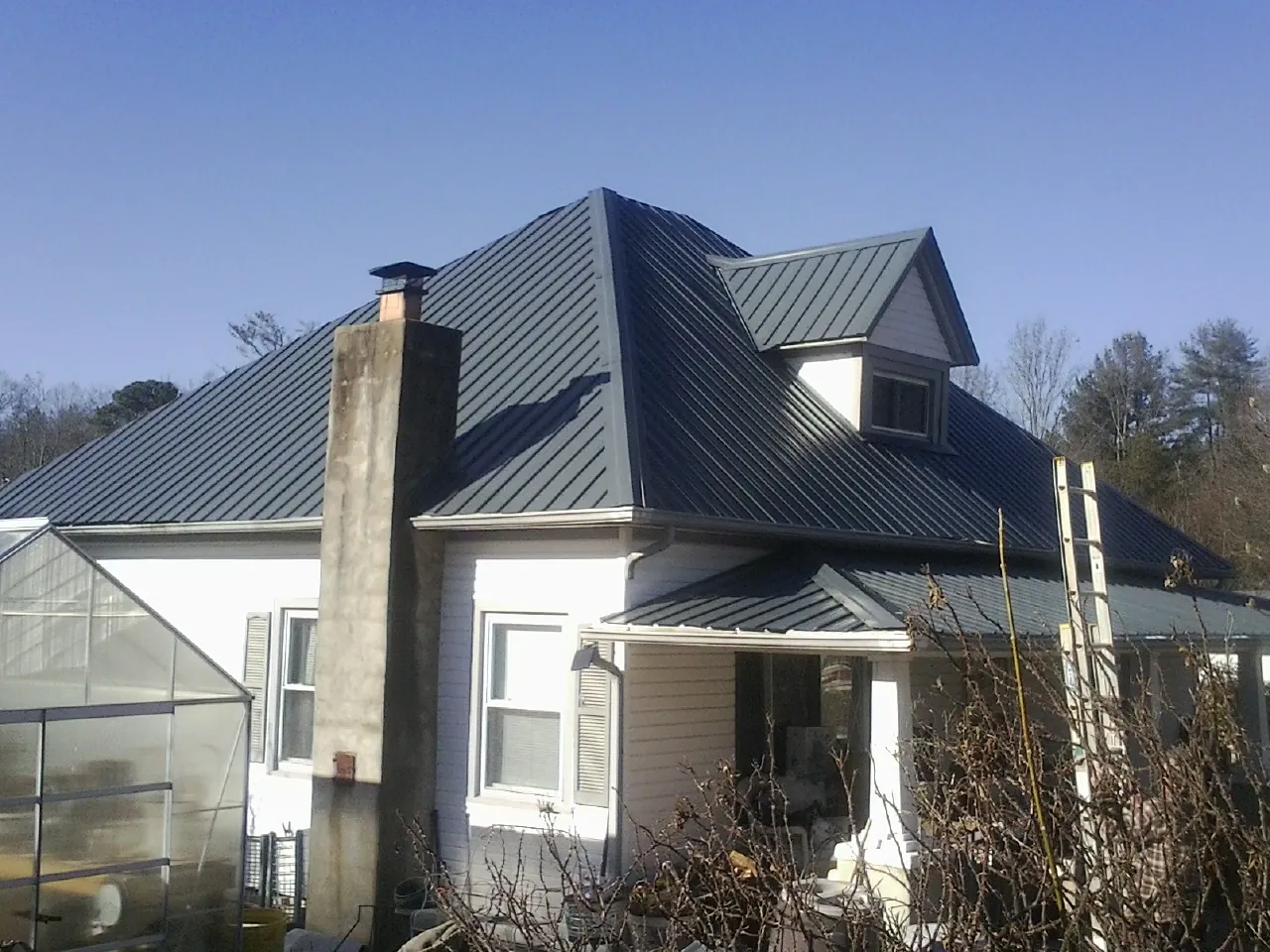 Dark blue standing seam metal roof on a white farmhouse with dormer — Slate & Tile Roof Repair by Roofing Brothers in Hollis