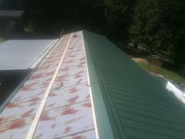 Old rusted panels beside newly installed green metal roofing — Wind Damage Roof Repair by Roofing Brothers in Hollis
