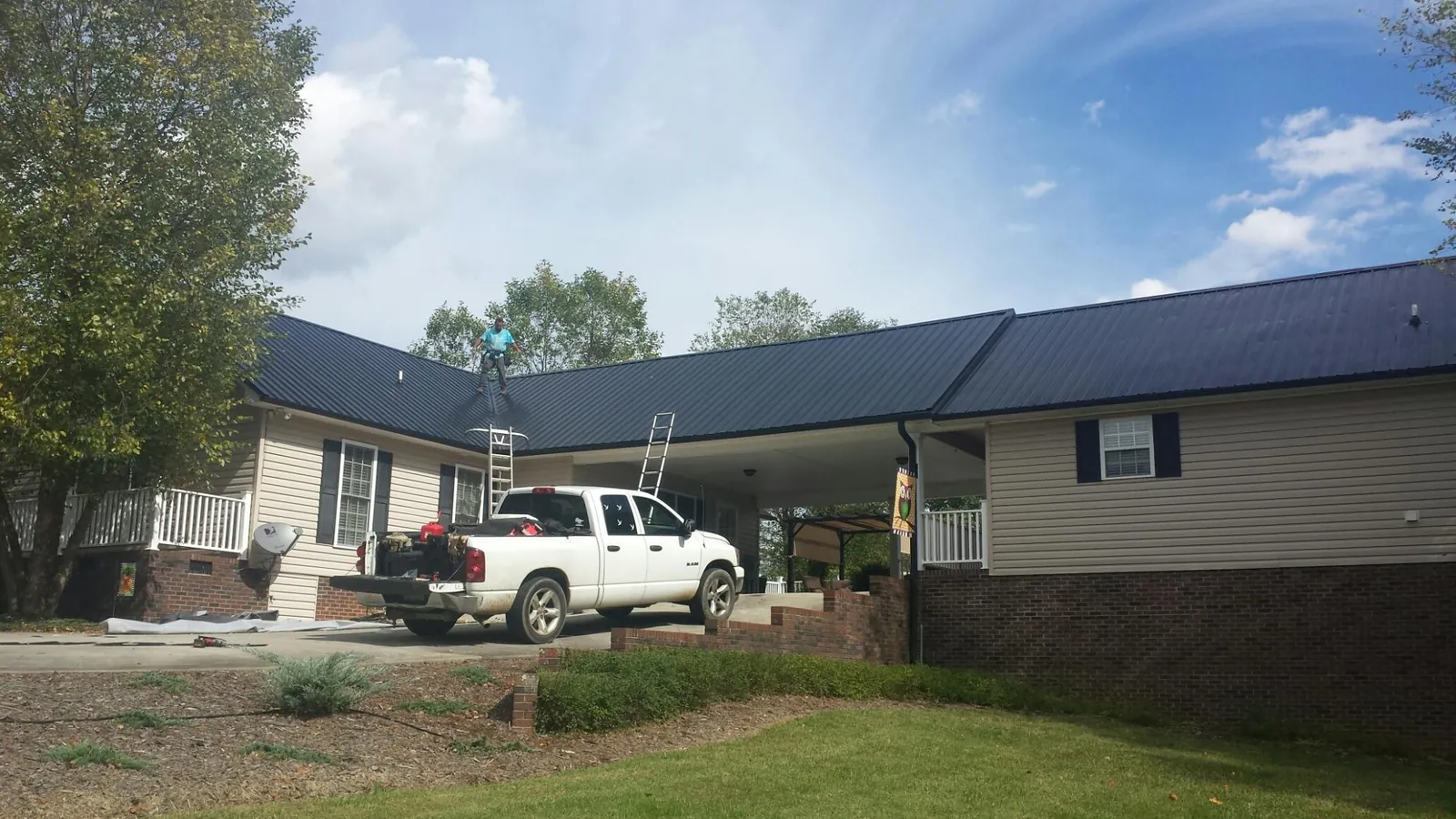 Black metal roof over a home and attached breezeway with ladders set in Hollis