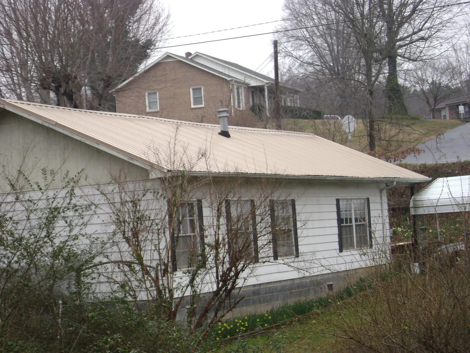 Tan metal roof on a white sided house set into a hillside — Commercial Roofing by Roofing Brothers in Hollis