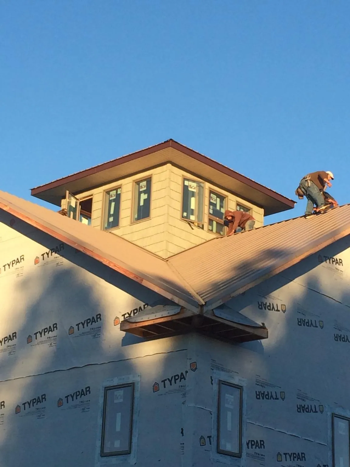 Roofers working around a rooftop cupola on a new metal roof at sunset — Roof Waterproofing in Hollis by Roofing Brothers